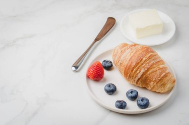 Beyaz kasede böğürtlenli kruvasan ve beyaz masada tereyağı bıçağı. Uzayı kopyala Sağlıklı kahvaltı.