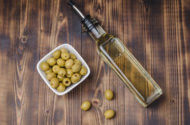 Ahşap arka planda beyaz bir kasede cam zeytinyağı ve zeytin yağı şişesi. Üst Manzara. Organik zeytinyağı konsepti