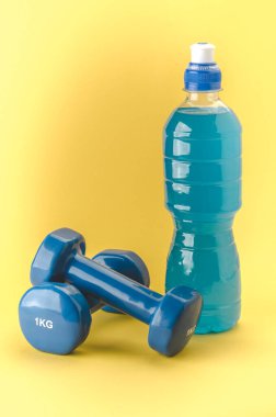 Halterli spor konsepti ve sarı arka planda mavi halterler ve şişe..