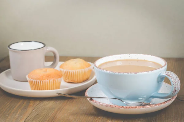 Coffee break. Muffins and blue mug with cappuccino and cream in a small cup for breakfast on a wooden table. Background with copy space