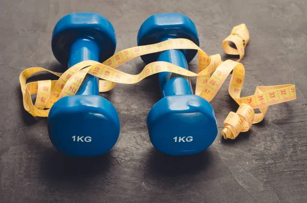 Dumbbells and measuring tape/fitness concept with blue dumbbells and measuring tape on a dark background