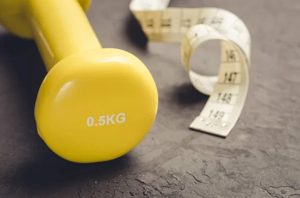 yellow dumbbell and measuring tape/fitness concept with yellow dumbbell and measuring tape on a dark background. Selective focus