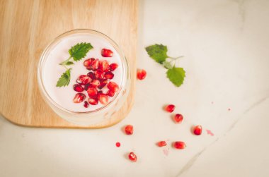 Yoğurt. Kuru üzümlü yoğurt ve tahta tepside nane şekeri ve beyaz bir masada dağınık nar tohumları. Üst Manzara. Tatlı tatlı.
