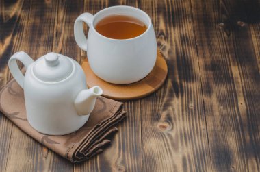 Bambu destekli beyaz bardak ve tahta bir masanın üzerindeki peçetede çaydanlık, kopyalanmış uzay.