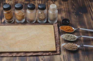 Kaşıklar içinde çeşitli baharatlar, yuvarlak kesim tahtaları ve ahşap arka planda pişirme aletleri..