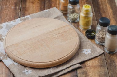 Çeşitli baharatlar, tahta kesme tahtası ve ahşap arka planda pişirme aletleri.