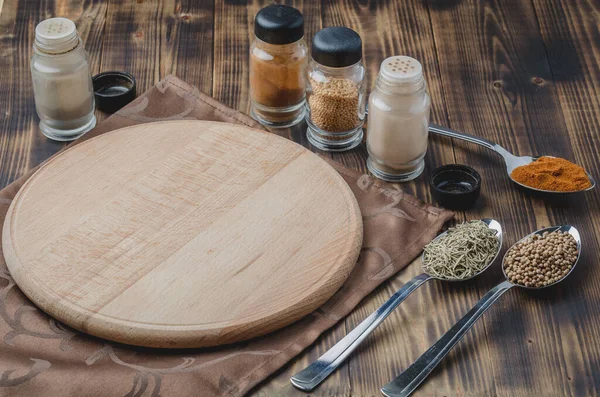 Çeşitli baharatlar, tahta kesme tahtası ve ahşap arka planda pişirme aletleri.