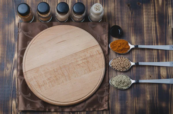 Kaşıklı çeşitli baharatlar, tahta kesme tahtası ve ahşap arka planda pişirme aletleri. Üst görünüm 