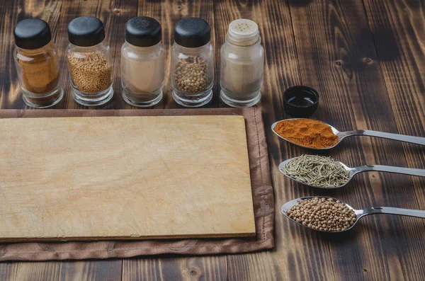Kaşıklar içinde çeşitli baharatlar, yuvarlak kesim tahtaları ve ahşap arka planda pişirme aletleri..