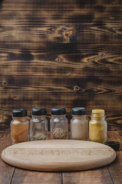 Çeşitli baharatlar, tahta kesme tahtası ve ahşap arka planda pişirme aletleri.