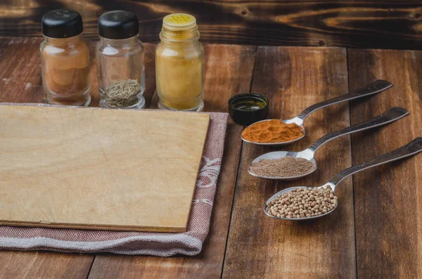 Kaşıklar içindeki çeşitli baharatlar, tahta kesme tahtaları ve ahşap masada pişirme aletleri.. 