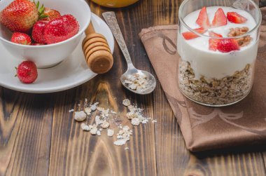 Tahta bir masada yoğurt, bal, fındık ve çilek..