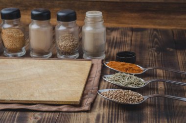 Çeşitli baharatlar, tahta kesme tahtası ve ahşap arka planda pişirme aletleri.