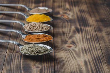 Tahta bir masada kaşıklardaki çeşitli baharatlar, kopyalanmış uzay