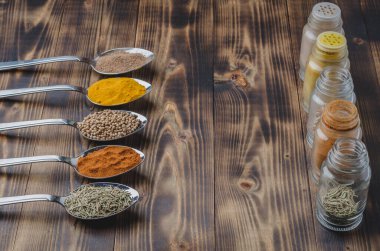 çeşitli baharatlar kaşıklarda ve cam kavanozlarda ahşap bir masada. Yemek pişirmek için gerekli malzemeler.