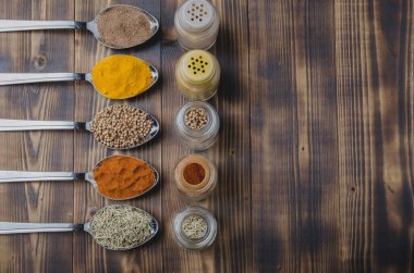 Renkli çeşitli baharatlar kaşıklarda ve tahta bir masada cam kavanozlarda. Üst görünüm ve telif alanı. Aşçılık arkaplanı.