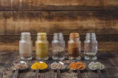 Renkli çeşitli baharatlar kaşıklarda ve tahta bir masada cam kavanozlarda. Aşçılık arkaplanı.