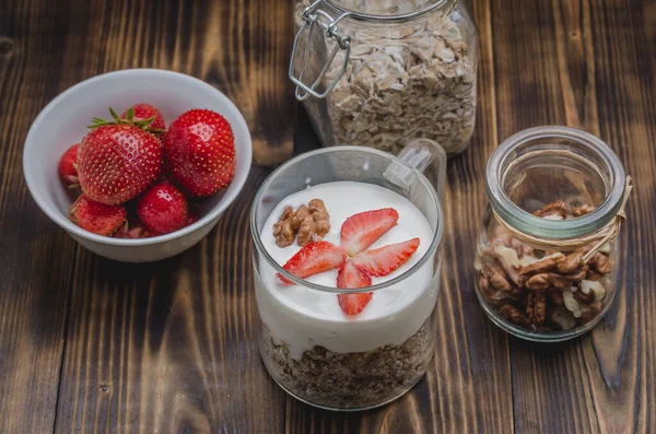 Sağlıklı kahvaltı. Yoğurt, taze çilek, ev yapımı granola ve ahşap bir masada açık cam kavanozda ceviz.