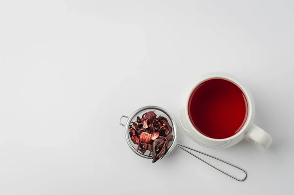 Beyaz fincanda kırmızı amber çayı ve beyaz arka planda izole edilmiş kuru çiçek, üst görünüm ve telif alanı