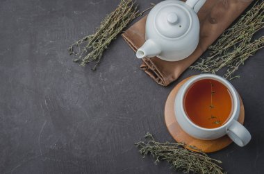 Kekik çayı beyaz bir fincanda ve çaydanlık siyah bir taş masada. Kopyalama alanı ve üst görünüm