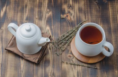Kekik çayı. Bambu destekli beyaz bardak ve tahta bir masanın üzerindeki peçetede çaydanlık. Üst görünüm