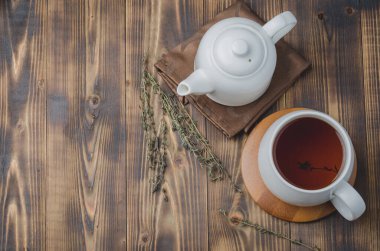 Kekik çayı. Bambu destekli beyaz bardak ve tahta bir masanın üzerindeki peçetede çaydanlık. Üst görünüm ve kopyalanma alanı