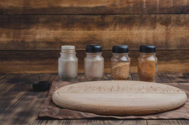 Çeşitli baharatlar, tahta kesme tahtası ve ahşap arka planda pişirme aletleri.