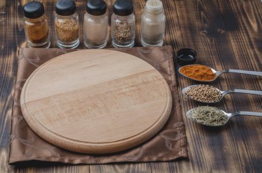 Çeşitli baharatlar, tahta kesme tahtası ve ahşap arka planda pişirme aletleri.