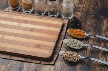 Kaşıklar içinde çeşitli baharatlar, yuvarlak kesim tahtaları ve ahşap masada pişirme aletleri..