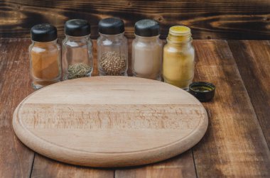 Çeşitli baharatlar, tahta kesme tahtası ve ahşap arka planda pişirme aletleri.