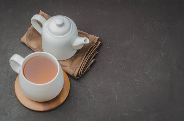 Тимьяновый травяной чай в белой чашке и чайник на черном каменном столе. Копировальное пространство и вид сверху
