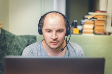 Genç adam dizüstü bilgisayarını kullanırken kulaklık takıyor. Genç adam evde dizüstü bilgisayarını kullanırken kulaklık takıyor.