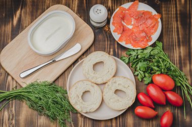 cooking of a food with round toast with cheese, red fish, tomatoes and vegetables/Healthy food with round toast, red fish, vegetables and cheese on wooden table. Top view.