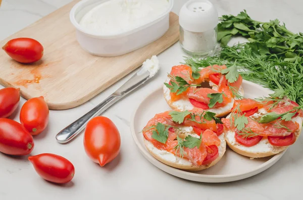 Healthy breakfast with round toast, red fish, vegetables and cheese/cooking of a breakfast with round toast with cheese, red fish, tomatoes and vegetables on a white table.