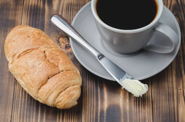 Kruvasan tereyağı bıçağıyla kahve molası ve koyu ahşap bir masada bir fincan sade kahve. Yakın çekim.