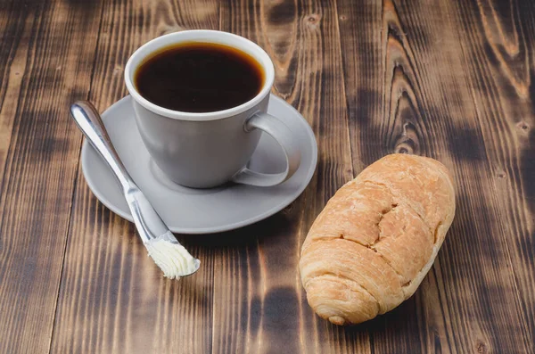 クロワッサンバターナイフでコーヒーブレイクと暗い木製のテーブルの上に黒いコーヒーカップ — ストック写真