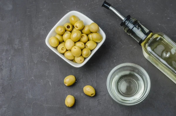 Fresh olives and oil in bottle on black stone background. Top view. Organic olive oil concept