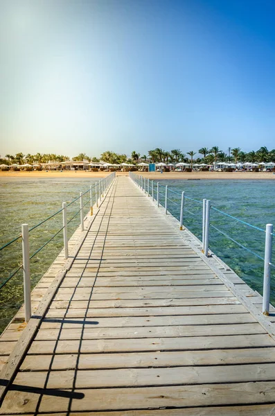 Wooden pier leading to the shore on a sunny day/beautiful wooden pier at the sea leading to the shore with blue sky