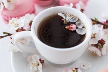 Bir fincan kahve ve bir şube beyaz bir arka plan üzerinde beyaz çiçek ile pembe bademli kurabiye. Fransız tatlı ve çiçek çiçeklenme kiraz. Sakura çiçek pembe acıbadem kurabiyesi ile yakın çekim.