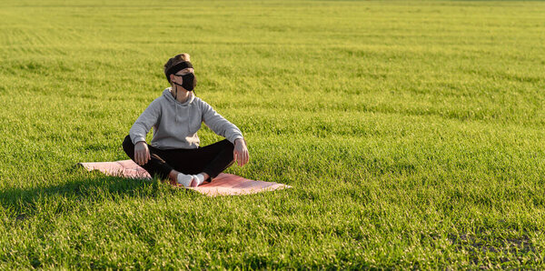 guy meditates in green field in medical mask