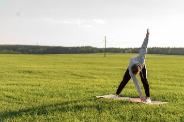 Yeşil alanda yoga yapan genç bir kadın.