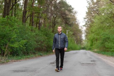 Genç adam parkta yürüyor.