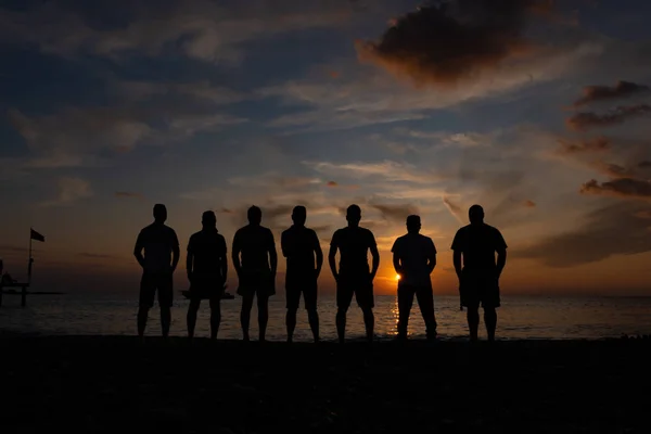 Silhouettes of men standing by the sea against the sunset. Royalty Free Stock Images