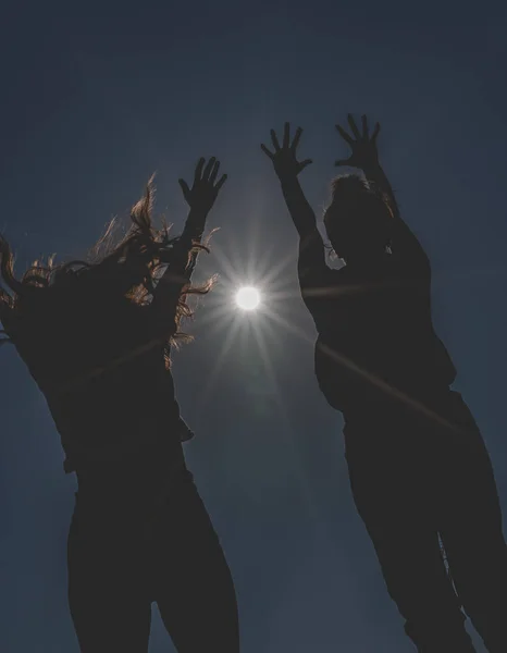 Silueta de dos jóvenes saltando hacia el sol con las manos arriba . — Foto de Stock
