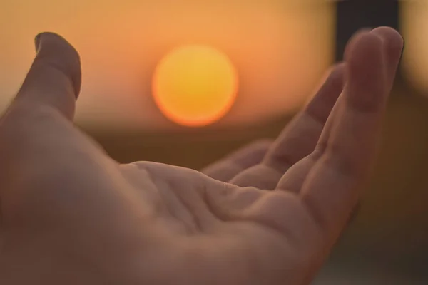 hand and fingers trying to touch sun, sunset background