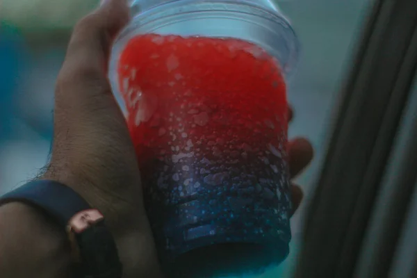Plastik bardakta kırmızı meyve suyu tutan el.