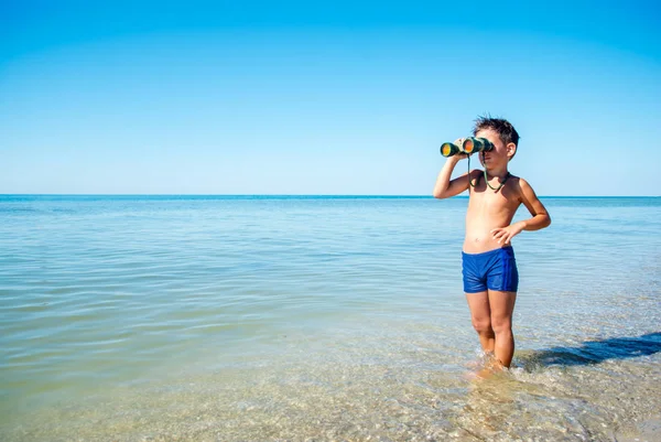 Boy looks through binoculars and sees sea — Stock Photo, Image