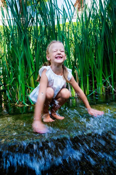 Mädchen sitzt im Wasser in der Nähe eines kleinen Wasserfalls — Stockfoto