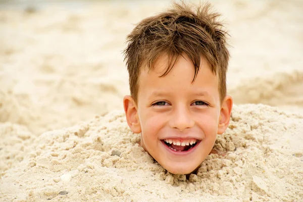 Liten pojke begravd i sanden på stranden — Stockfoto