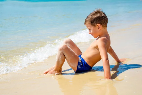 Pequeño niño solo sentado en la playa cerca del agua — Foto de Stock